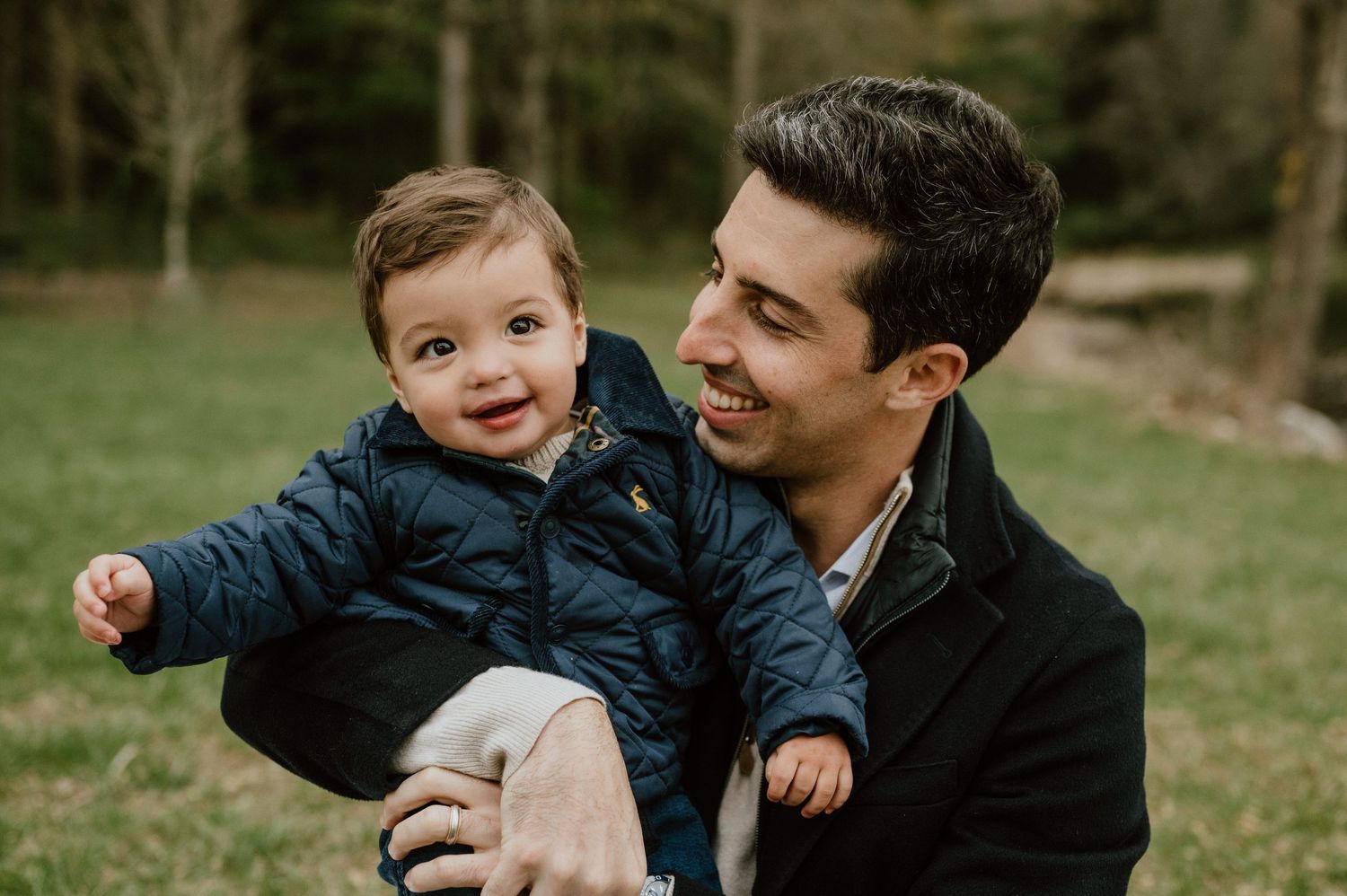 Candid outdoor moment of a young child in blue winter coat being held and smiling.