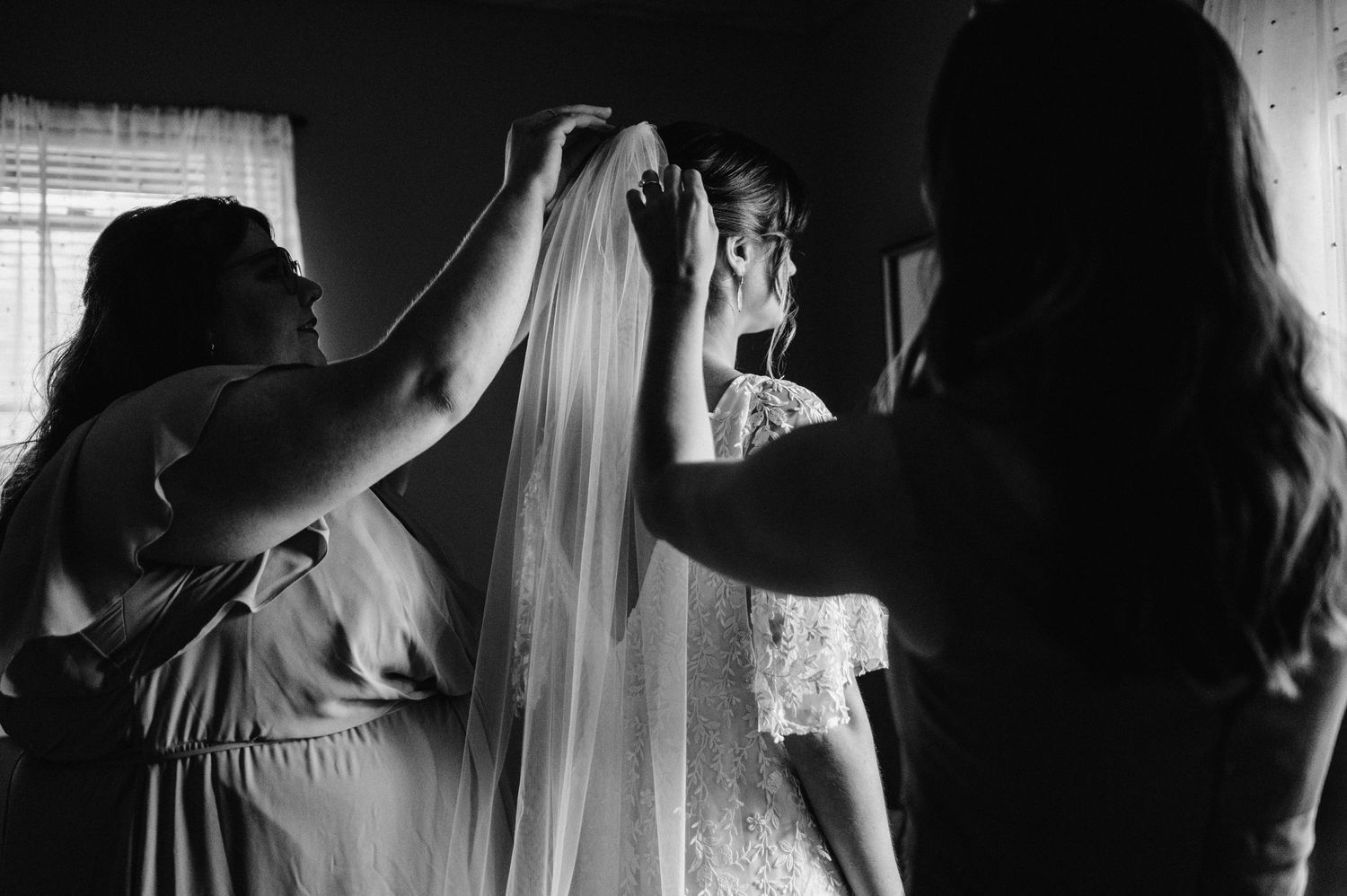 Black and white photo showing preparations with a wedding veil in a dimly lit room.