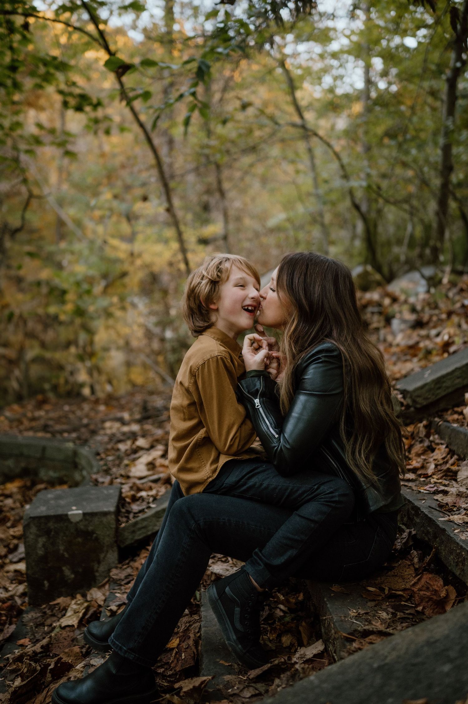 Two people share a joyful moment while sitting on wooden steps covered in autumn leaves.