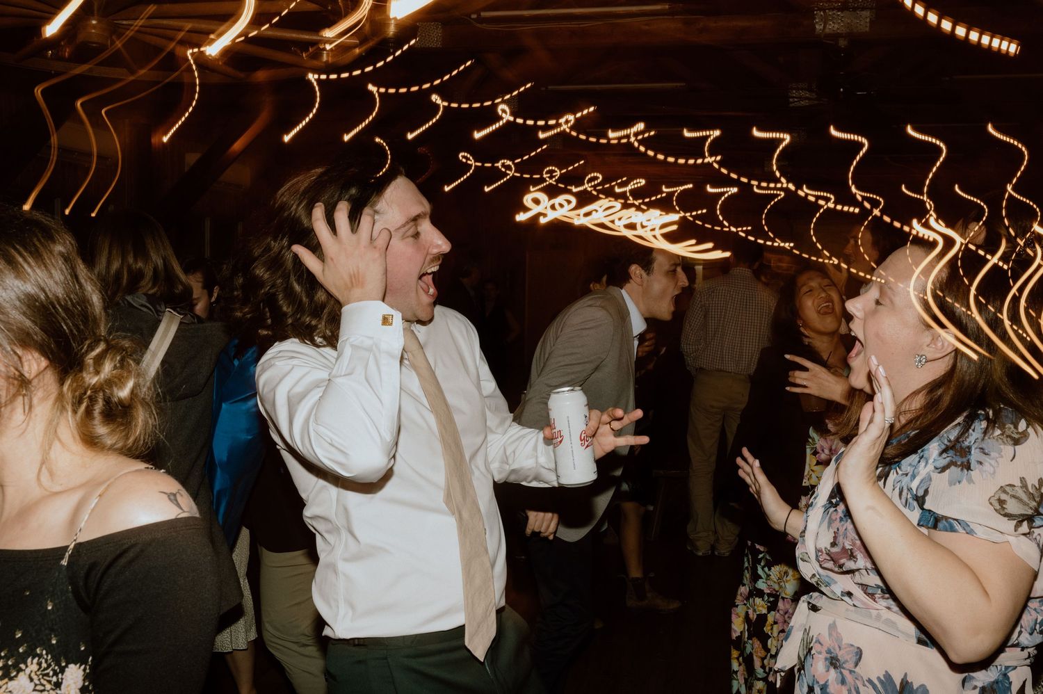 People celebrating enthusiastically under string lights at indoor party.