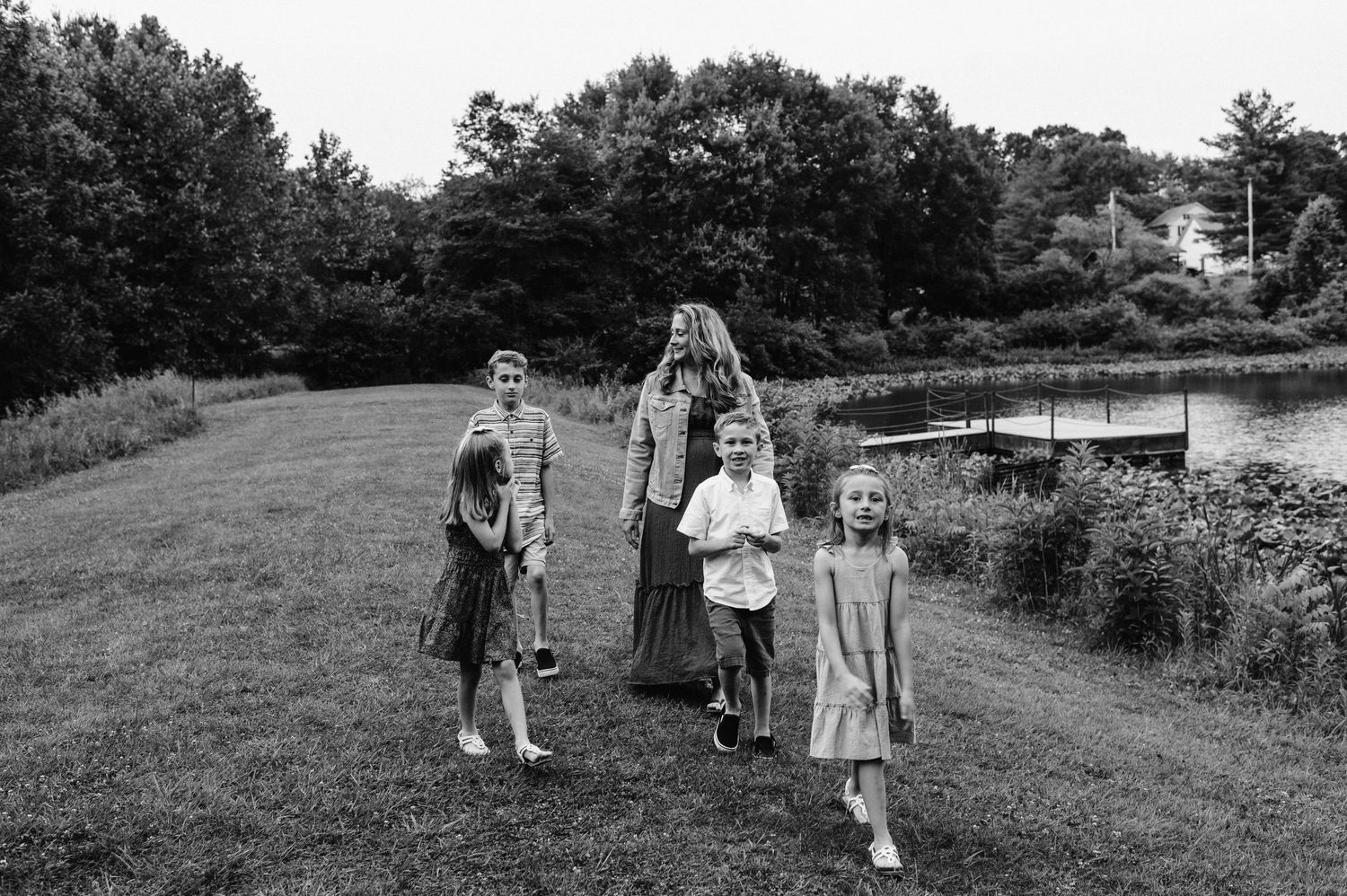 Black and white photo of family members walking together near a lake with trees in background.