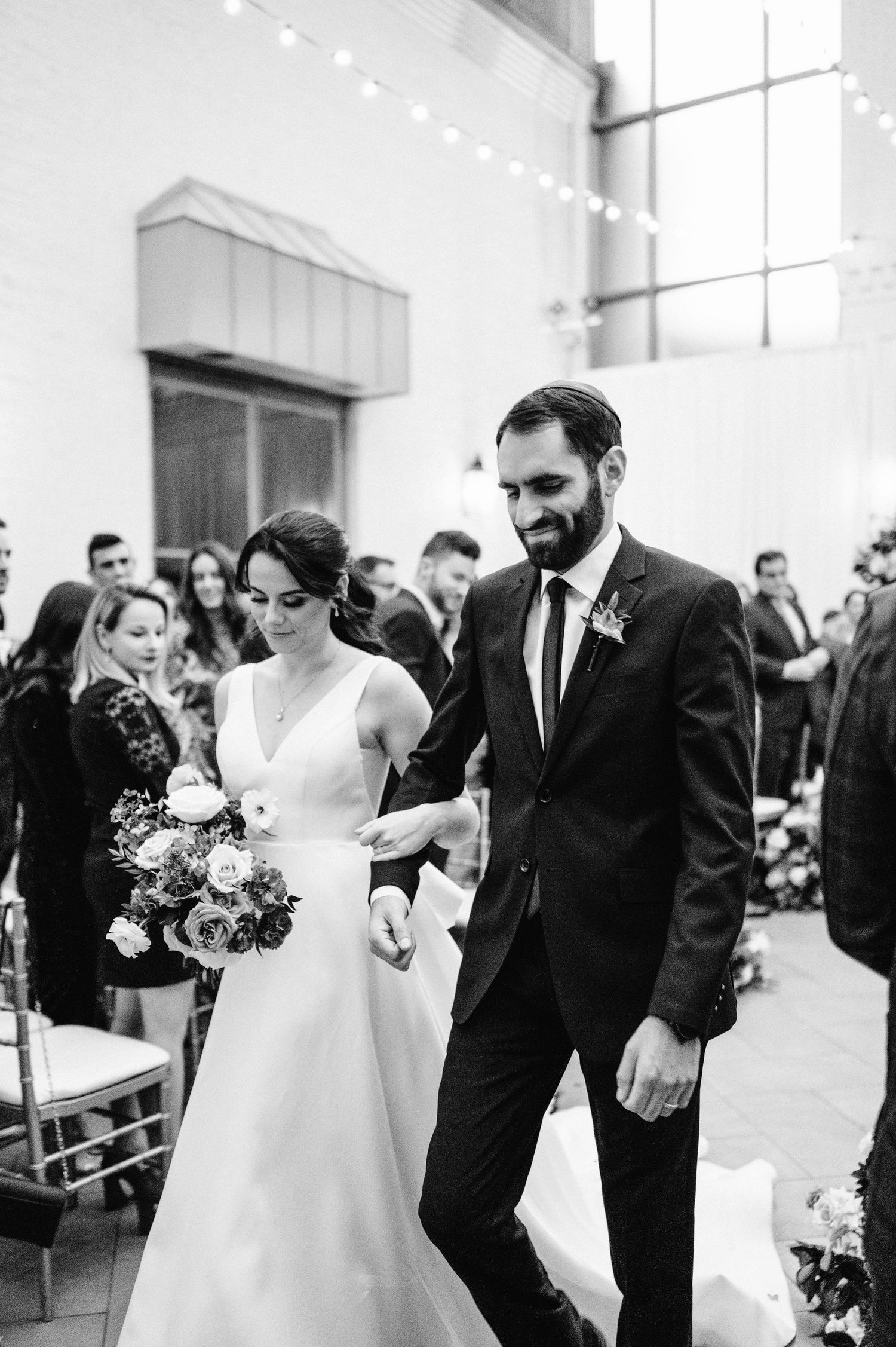 Indoor wedding ceremony exit with string lights and elegant decor.