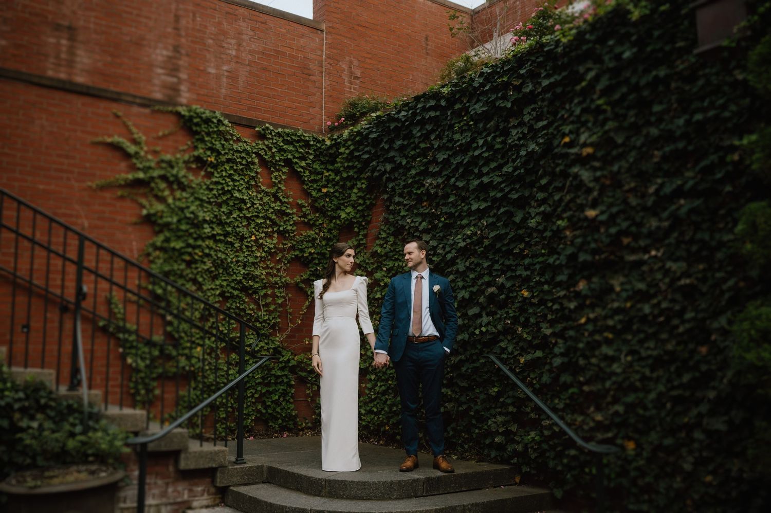Elegant couple poses on curved stone steps with ivy-covered wall backdrop.