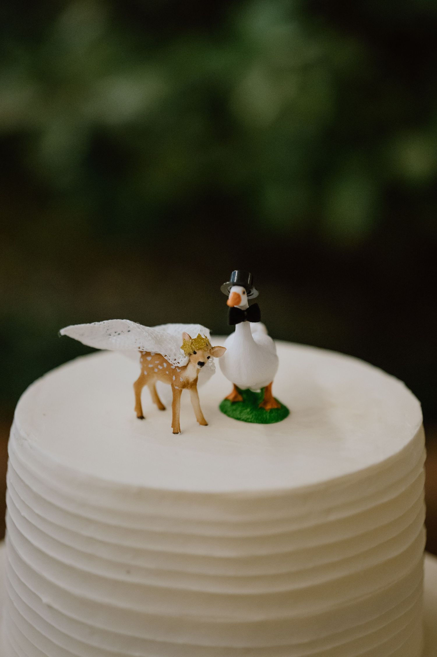 White wedding cake topped with miniature deer and penguin figurines.