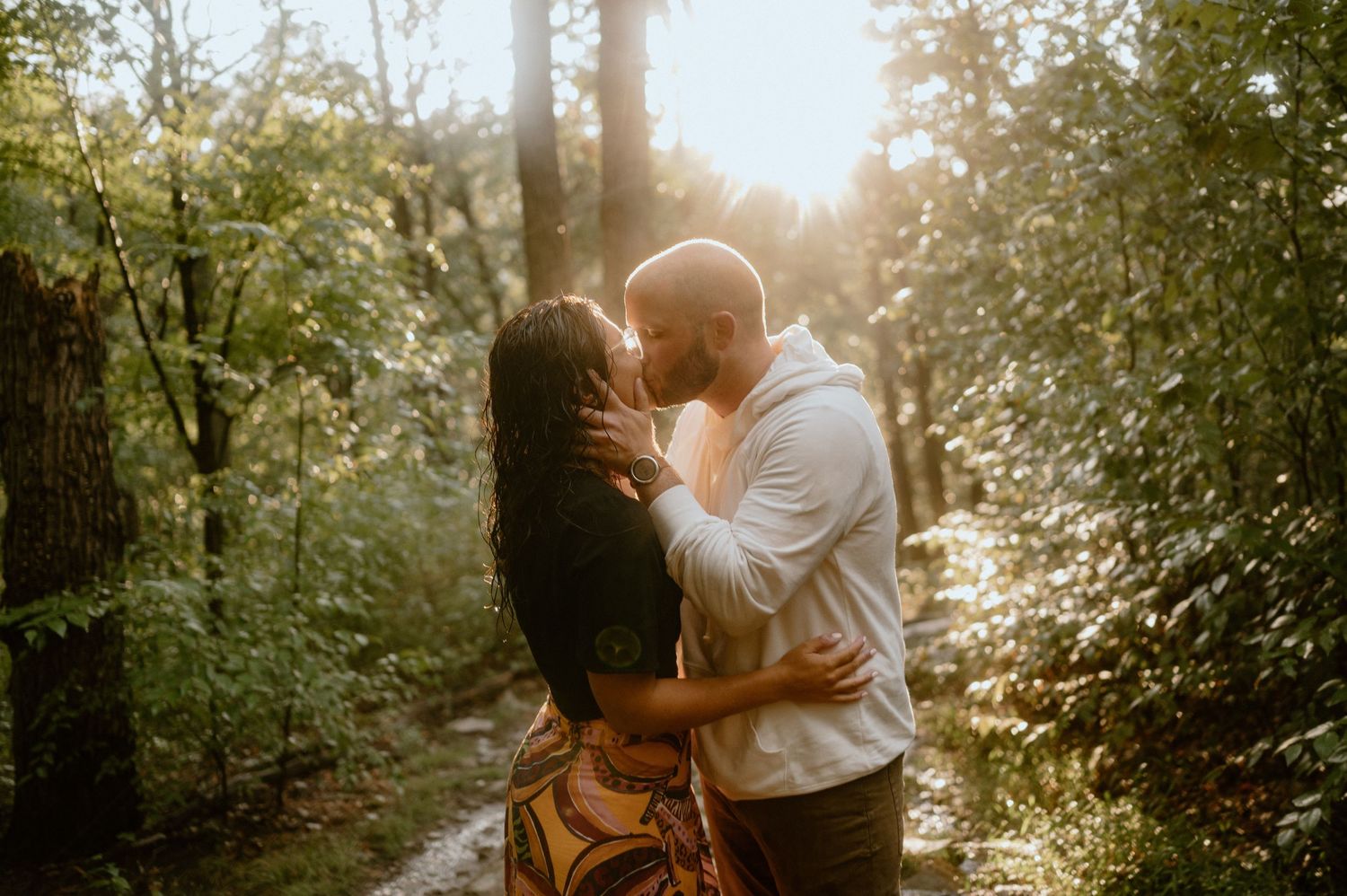 Golden sunlight filters through trees as couple shares romantic moment on forest path.