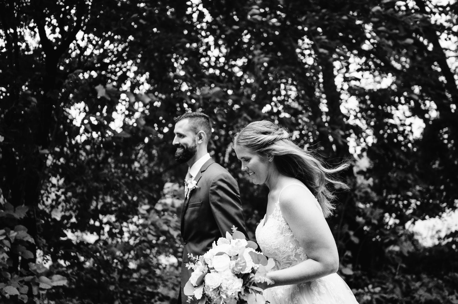 A black and white photo of newlyweds walking together outdoors with bride holding a bouquet.