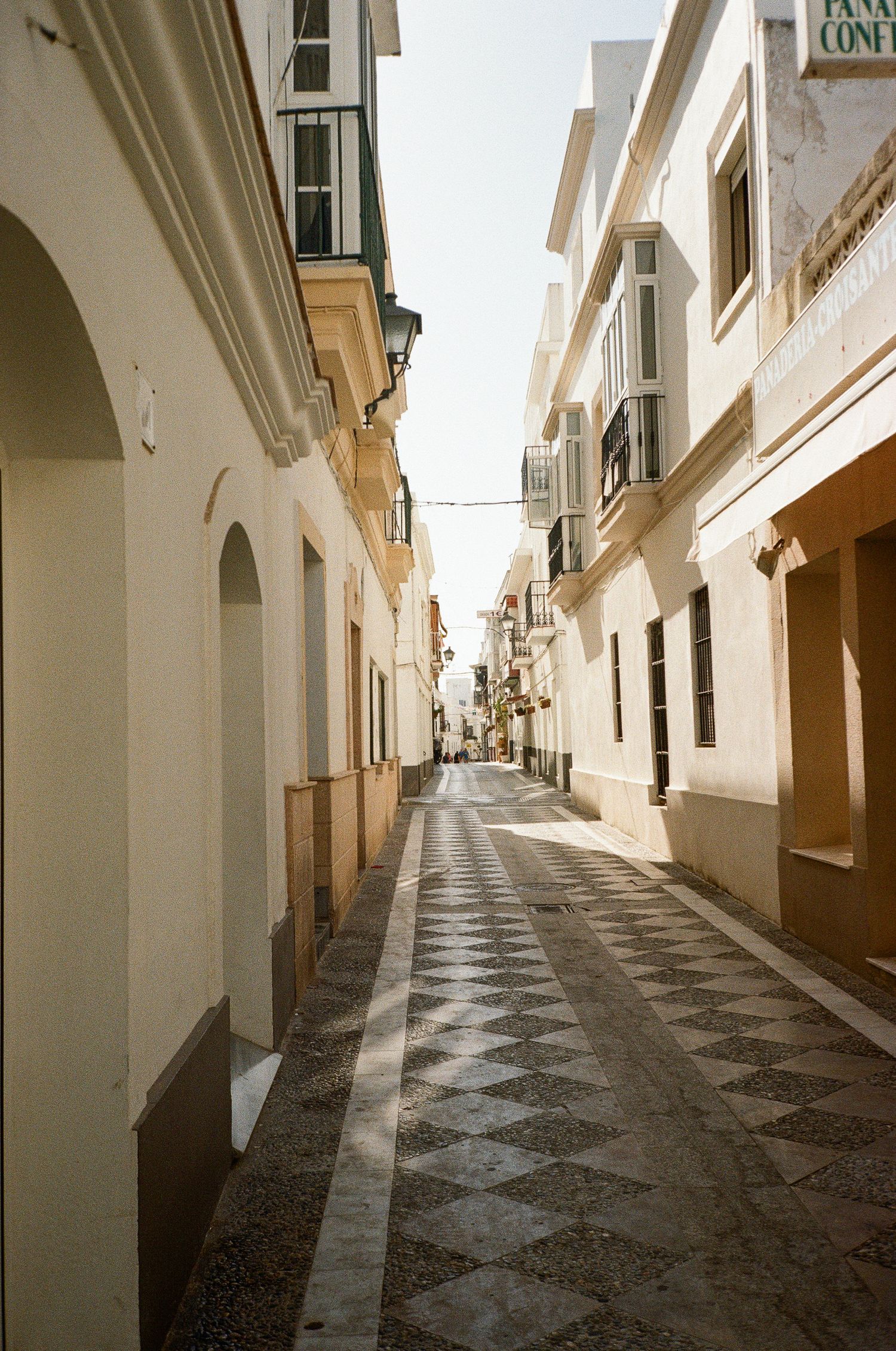 Narrow cobblestone street between white buildings with traditional Spanish architecture.