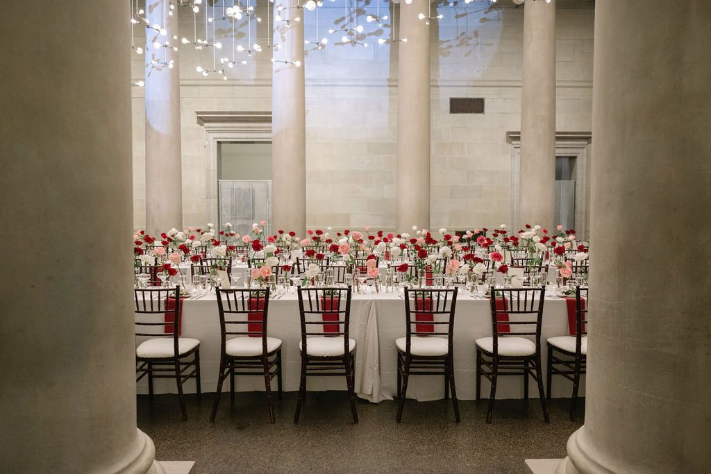 Elegant wedding reception hall with white columns and formal table settings arranged in long rows.