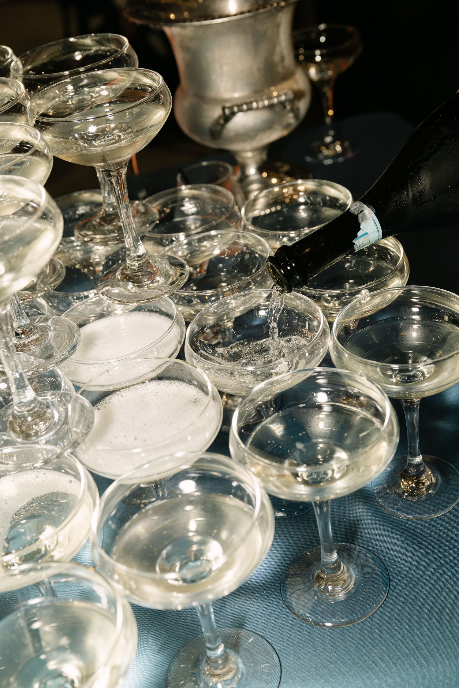 Elegant champagne coupe glasses arranged on a blue tablecloth with a silver ice bucket at a formal event.