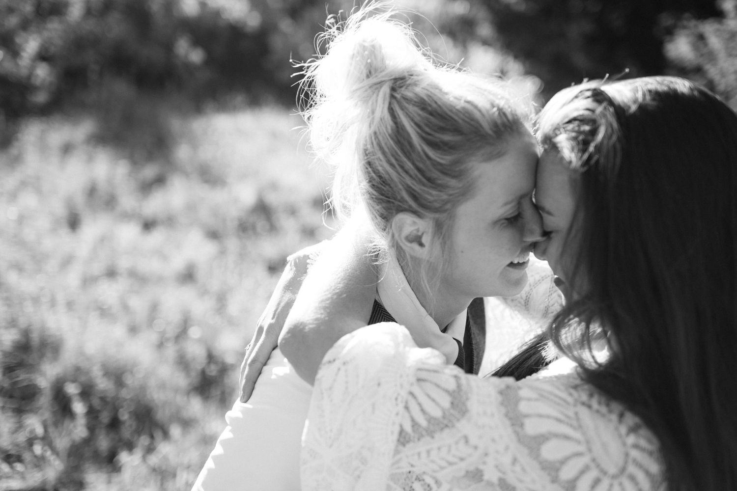 An intimate black and white portrait of two people sharing a tender moment outdoors.