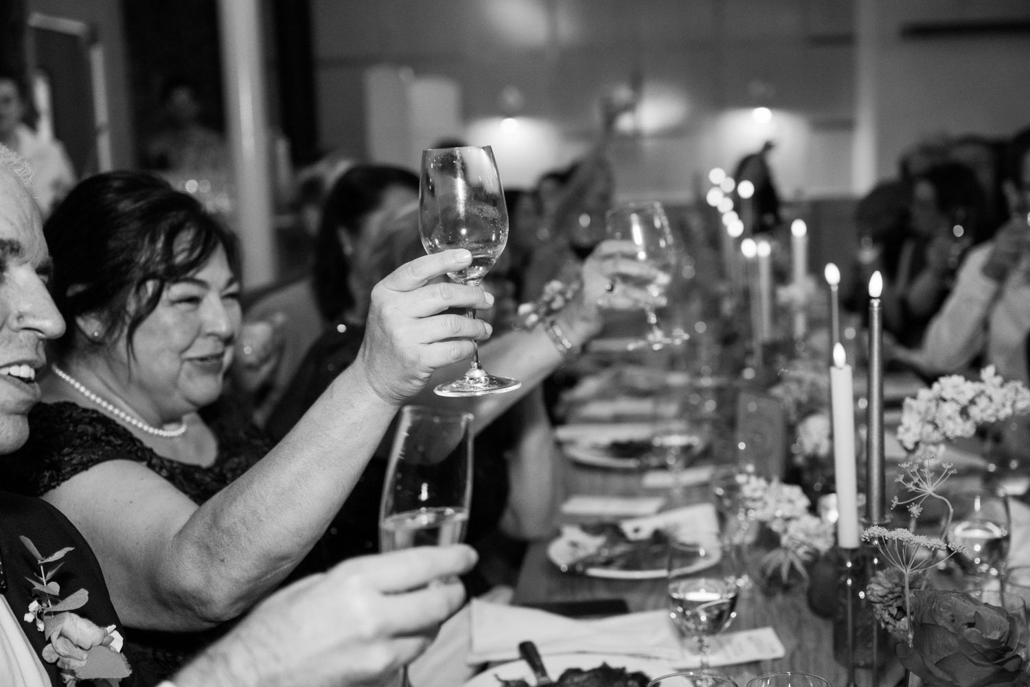 Wedding guests raise their glasses in a toast at a candlelit reception dinner.