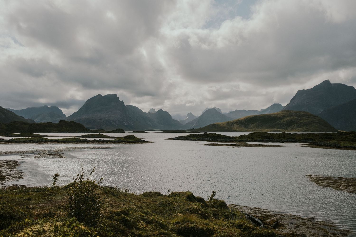 Dramatic mountain landscape reflected in calm waters of a Nordic fjord under cloudy skies.