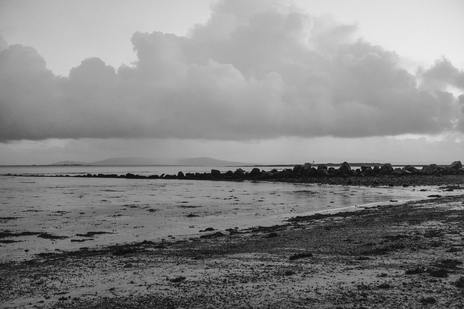Dramatic black and white seascape with stormy clouds over a rocky beach.