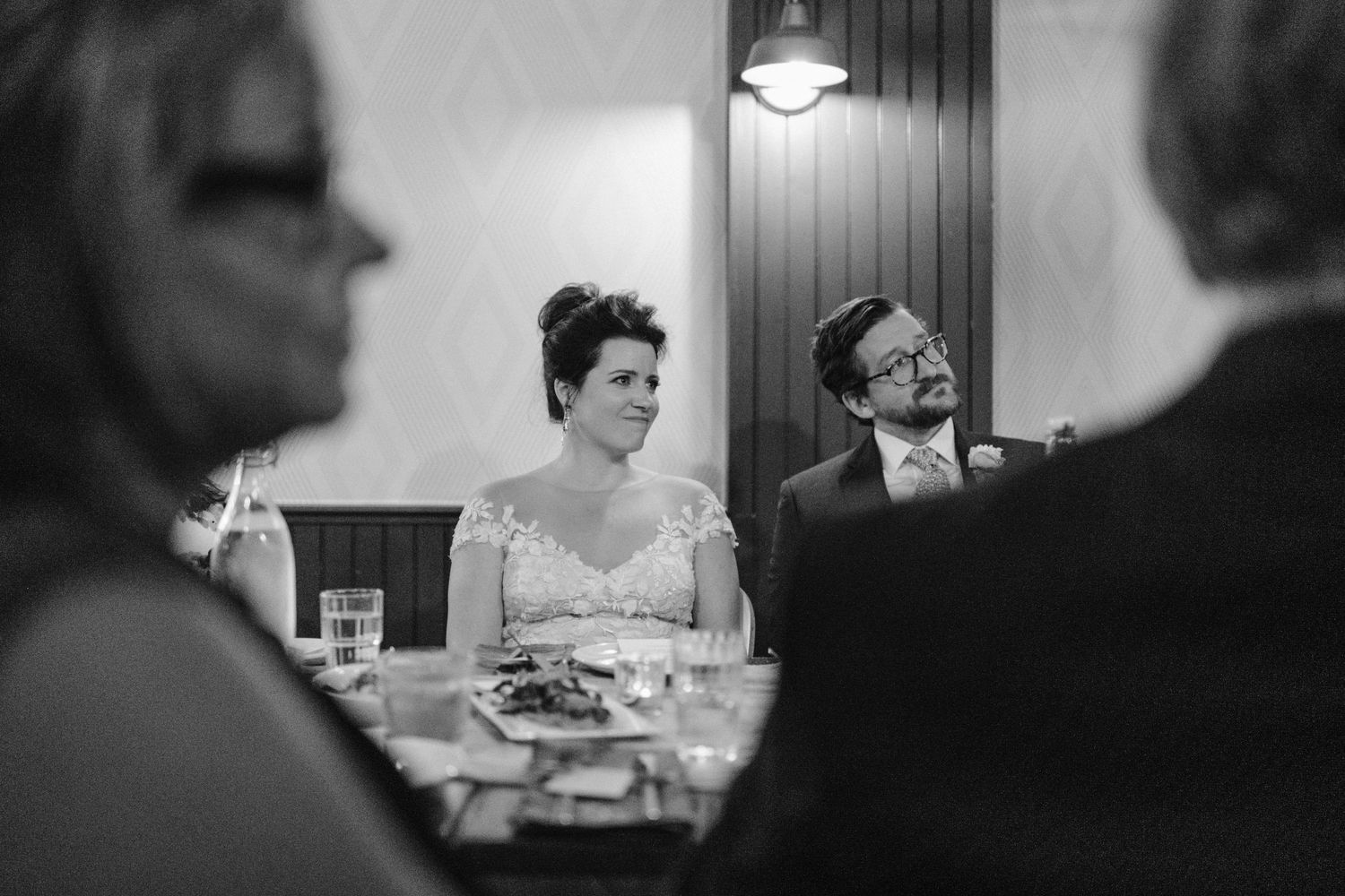 Black and white candid shot of guests during wedding dinner conversation.