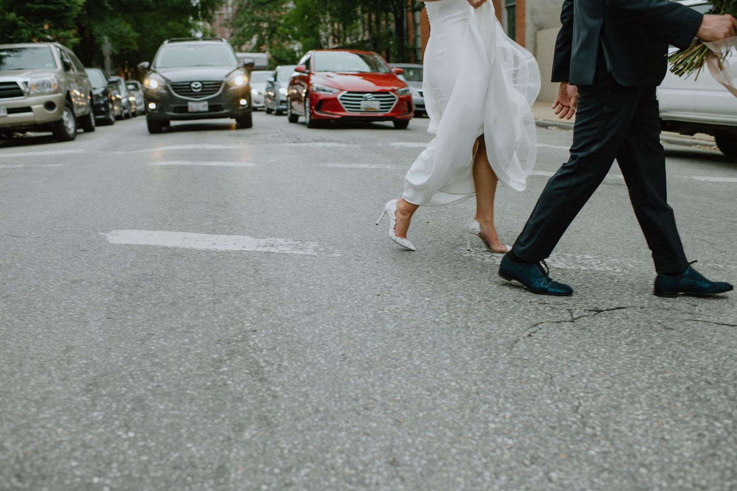 Ground-level view of bride and groom's feet walking across an urban street.