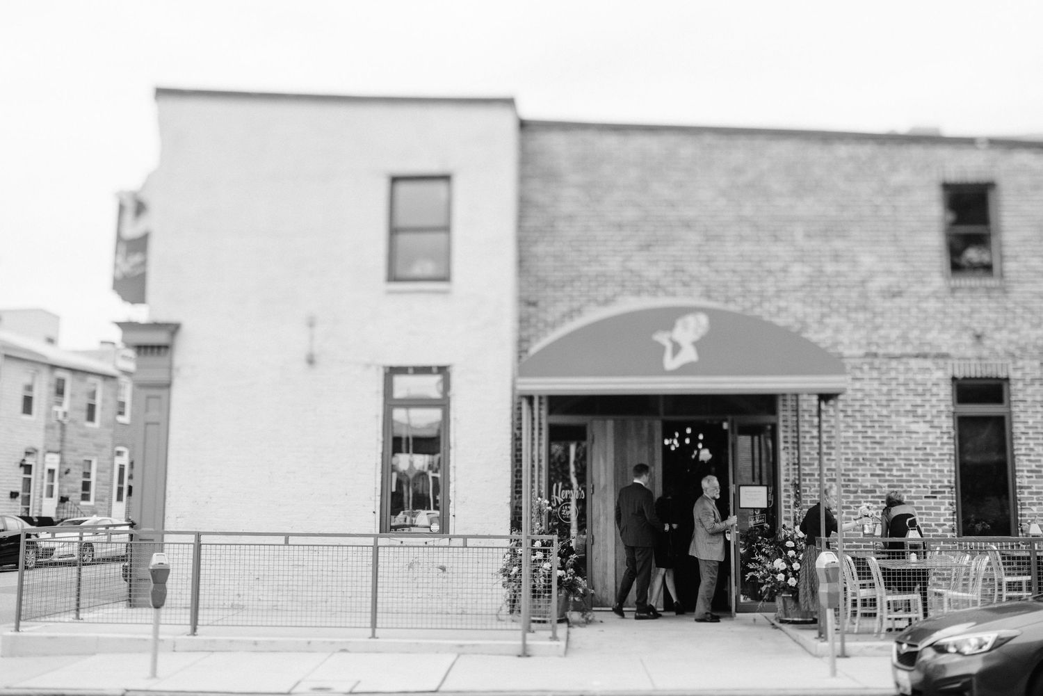 Black and white photo of guests gathered outside a brick building entrance with an awning.