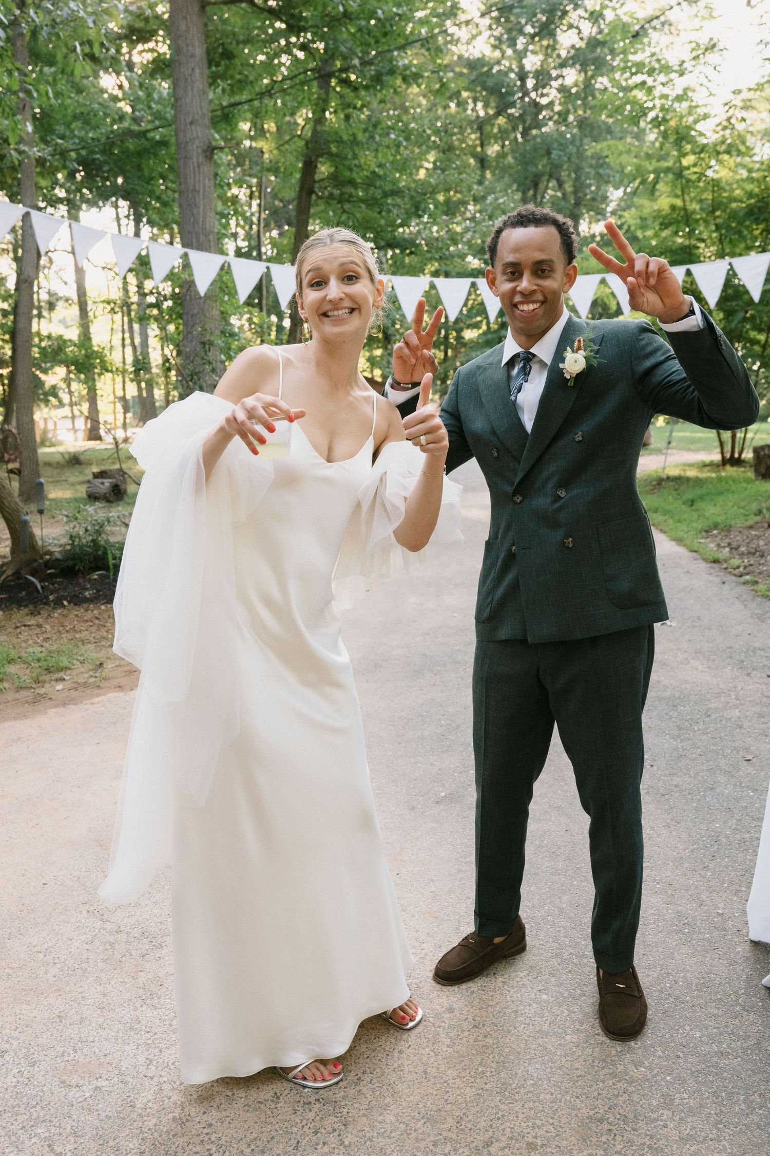 A couple celebrating joyfully on a path decorated with white bunting at an outdoor wedding.