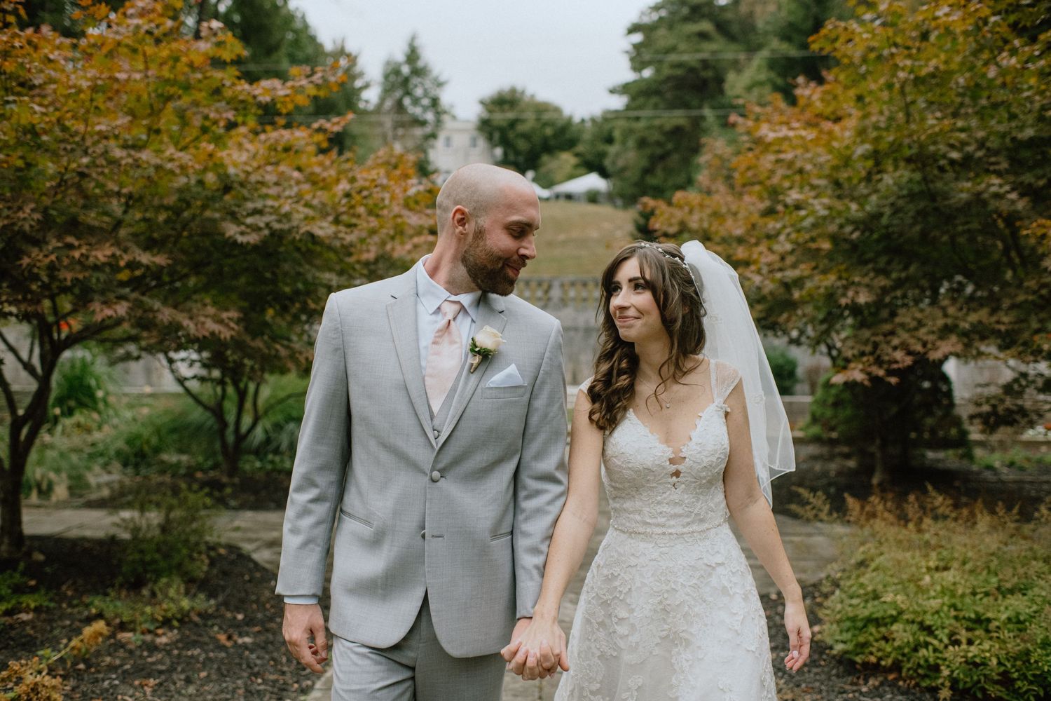 Newlyweds walking together through autumn foliage in a garden setting.