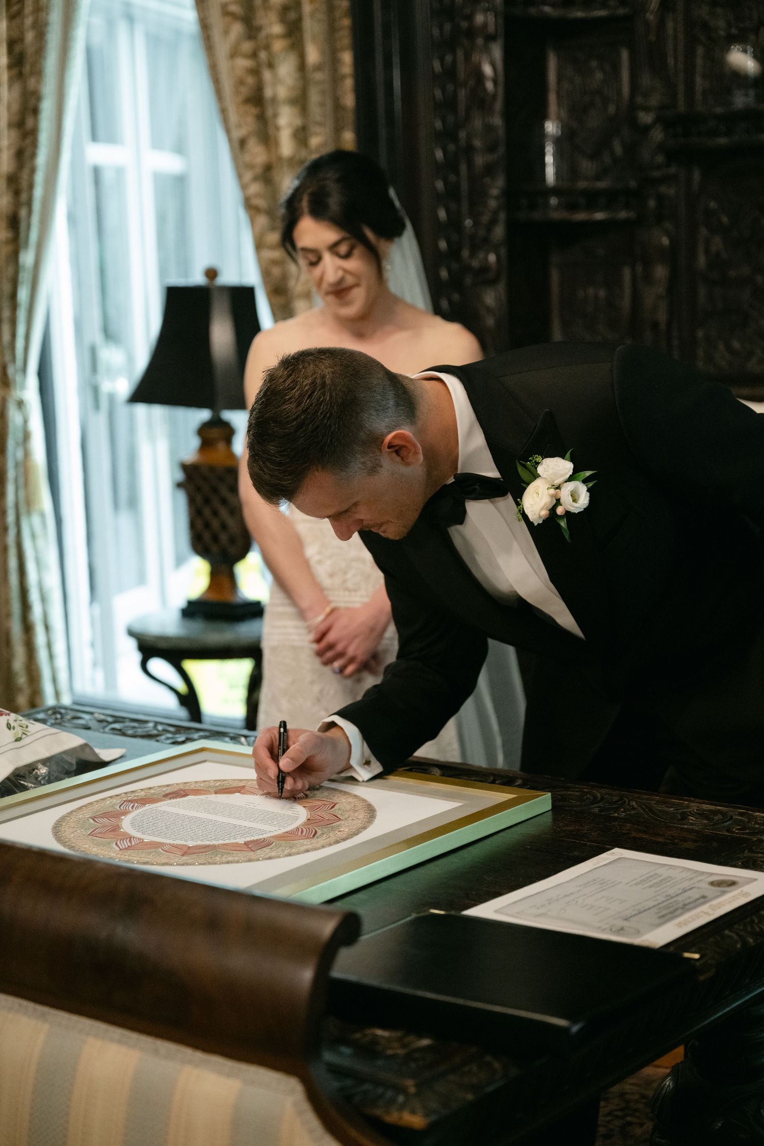 A couple signing their marriage certificate together in an elegant room with ornate decor.