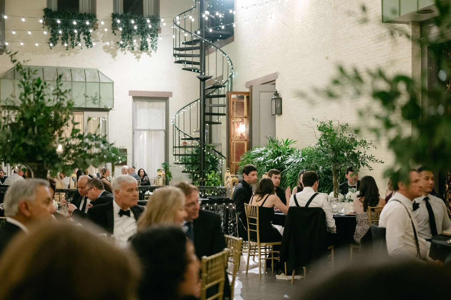 Wedding reception venue with spiral staircase and string lights above seated dinner guests.
