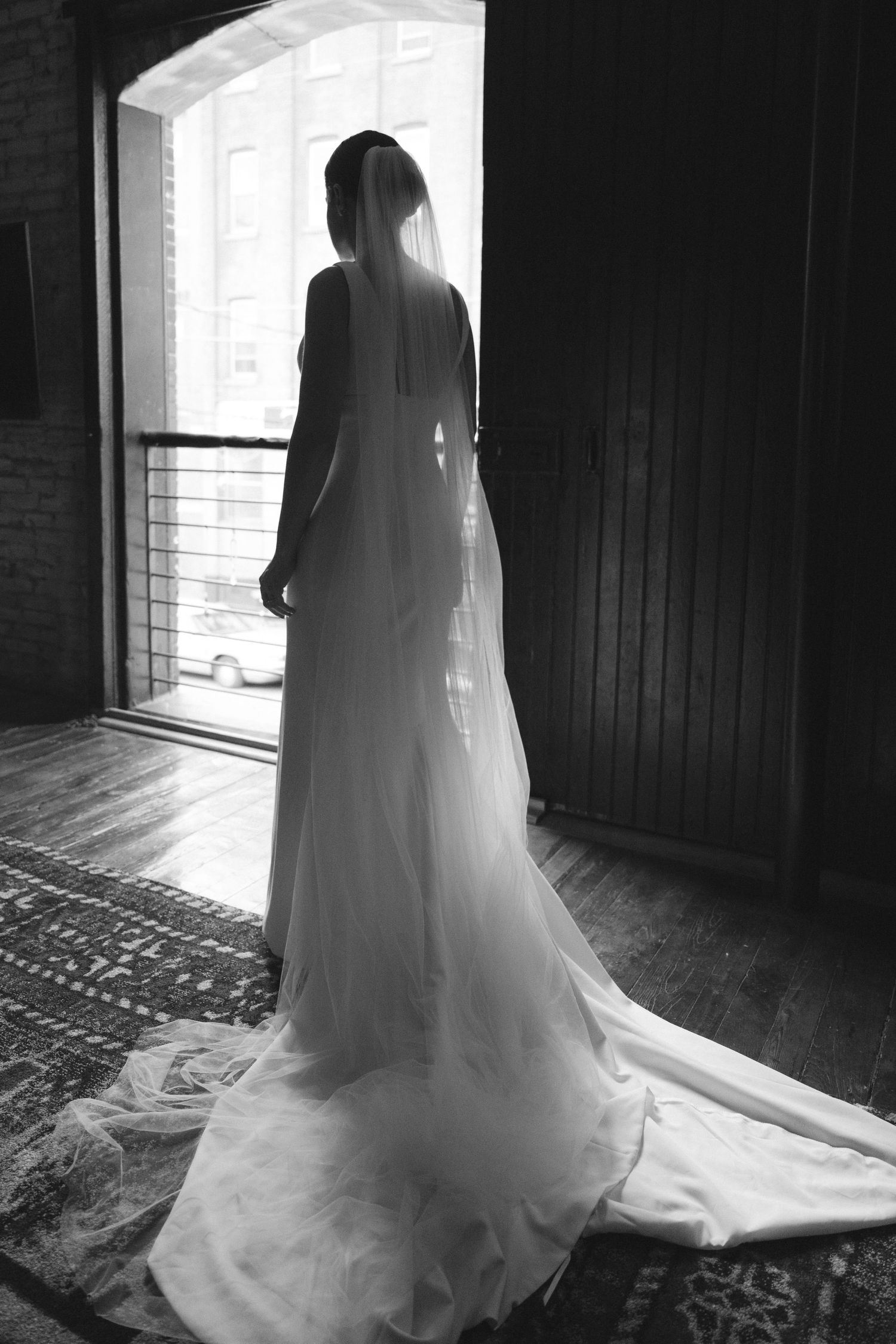 Dramatic backlit silhouette of flowing wedding dress train against bright window.