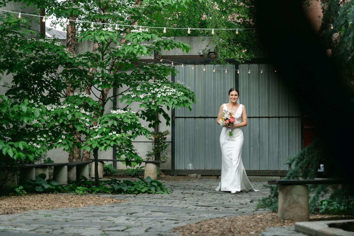 Garden courtyard with greenery and gray metal wall creates elegant outdoor portrait setting.