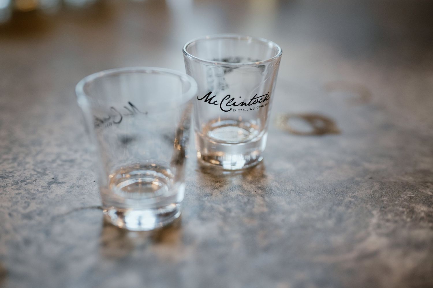 Two empty shot glasses on a textured surface with one glass labeled McCormick.