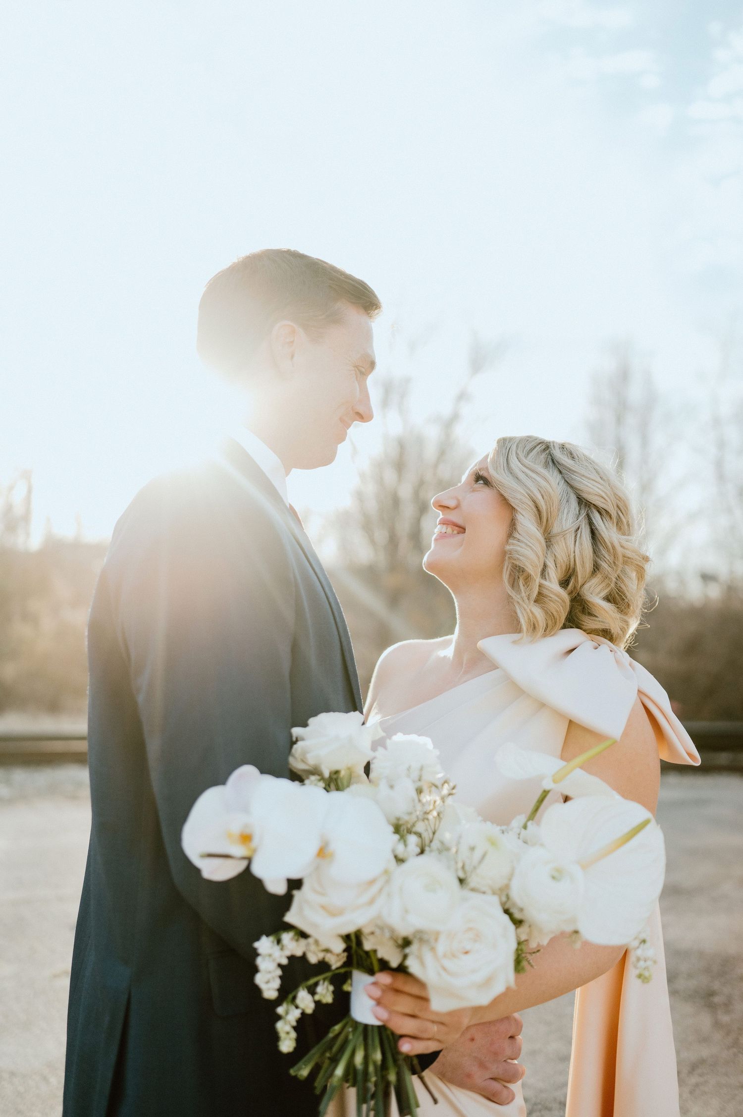 Romantic sunlit portrait of couple with white floral bouquet during wedding photoshoot.