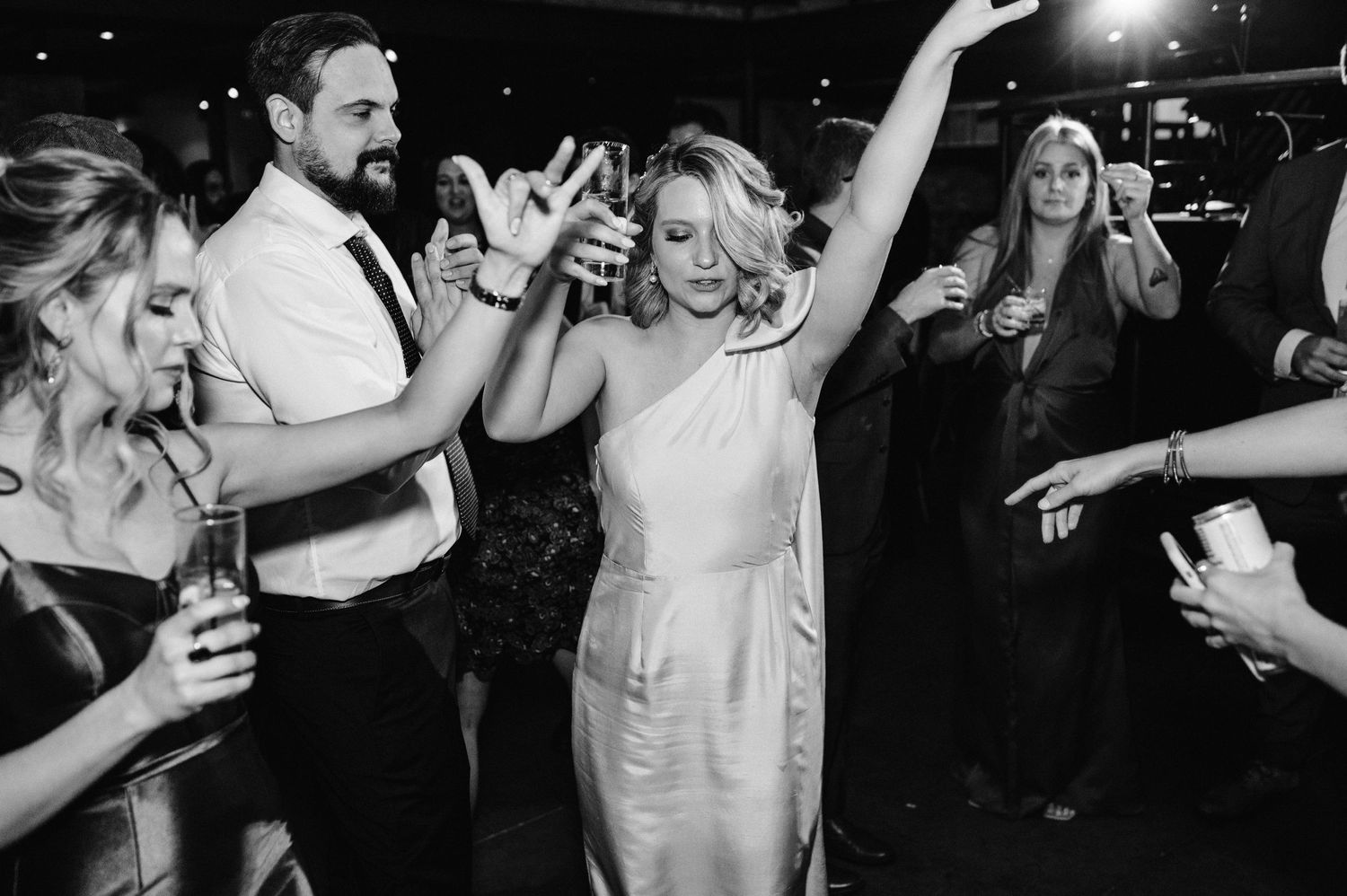 Wedding guests celebrate on the dance floor with arms raised in black and white.