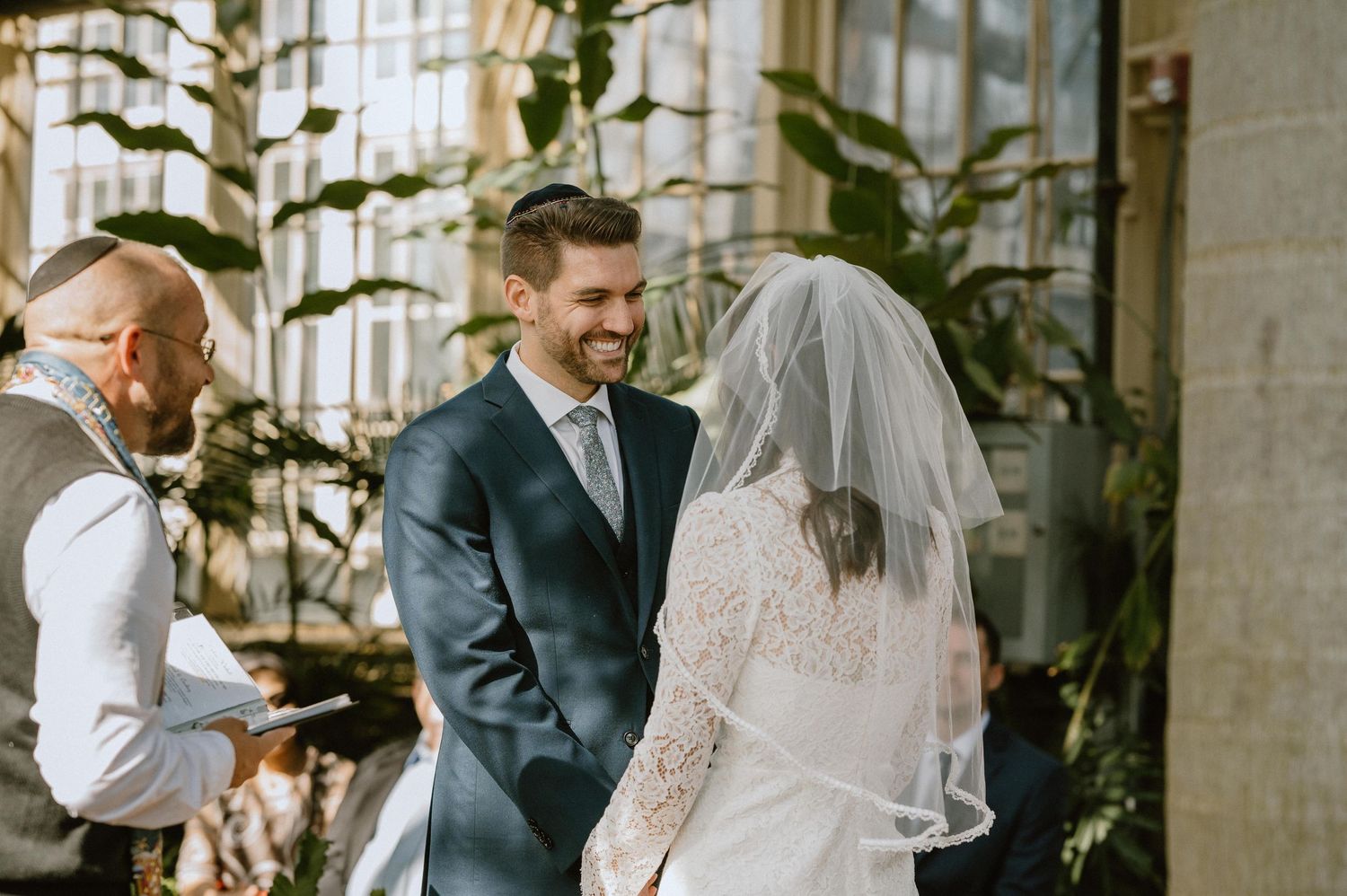 Jewish wedding ceremony taking place in bright greenhouse with tropical plants.