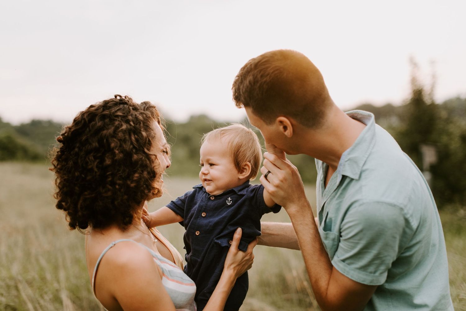 A joyful family moment captured in a field at sunset with their laughing baby.