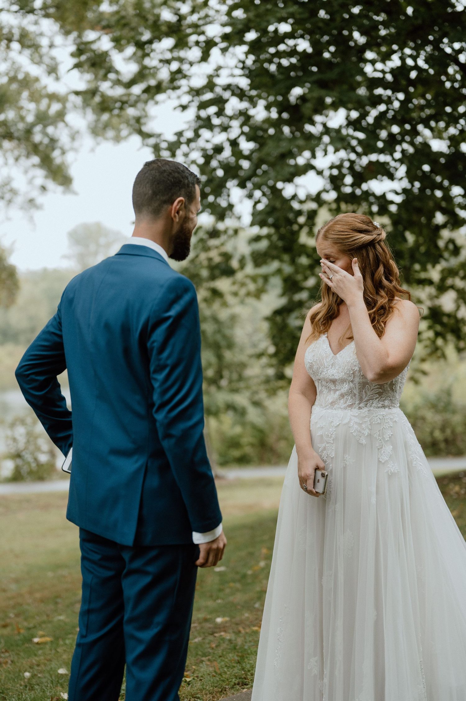Emotional outdoor wedding moment between couple in formal attire surrounded by trees.