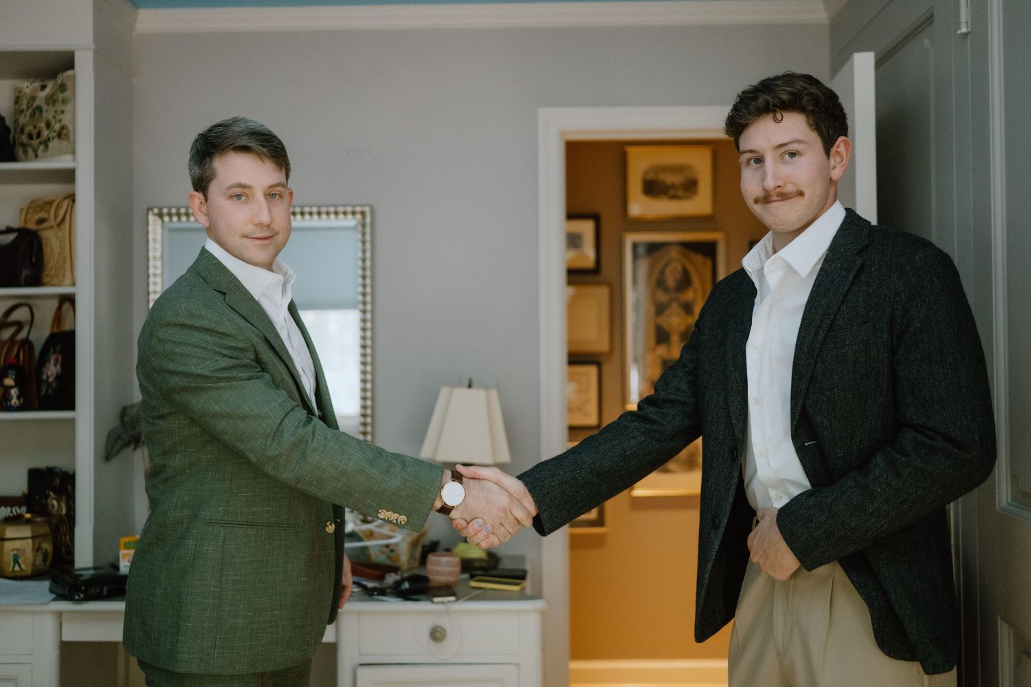 Two men in suits shake hands in a bright interior room setting.
