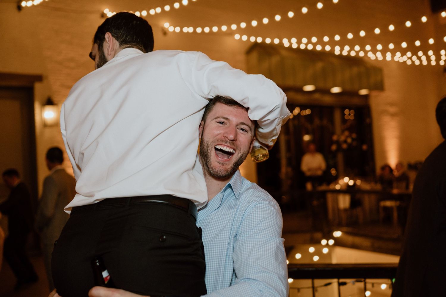 Wedding guests sharing a joyful moment on the dance floor under string lights.