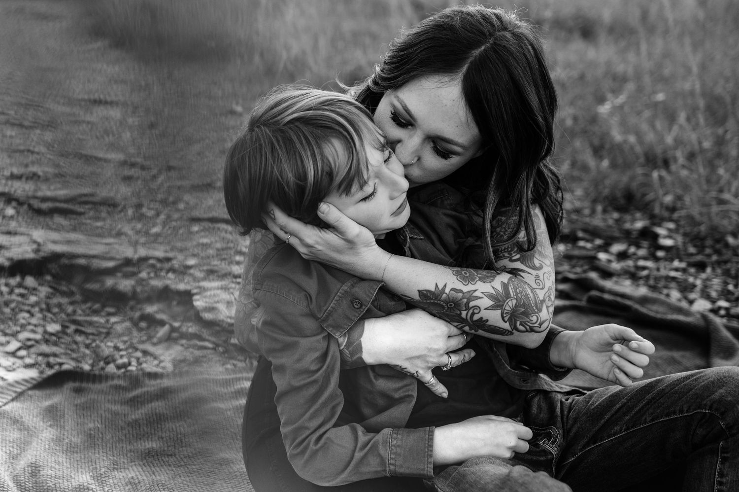 A black and white photo captures an intimate moment between parent and child on a blanket outdoors.