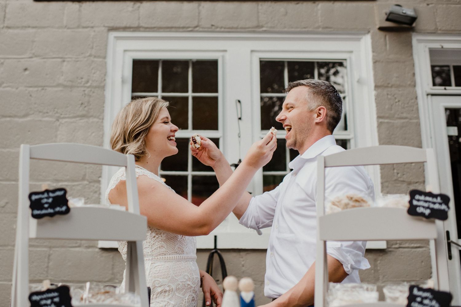A playful moment as a couple feeds each other cake outside a brick building.