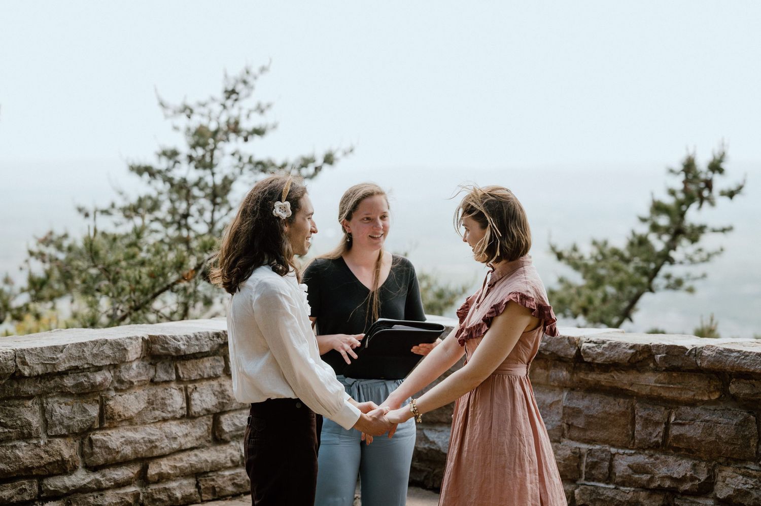 Three people sharing an intimate moment at a scenic mountain overlook.