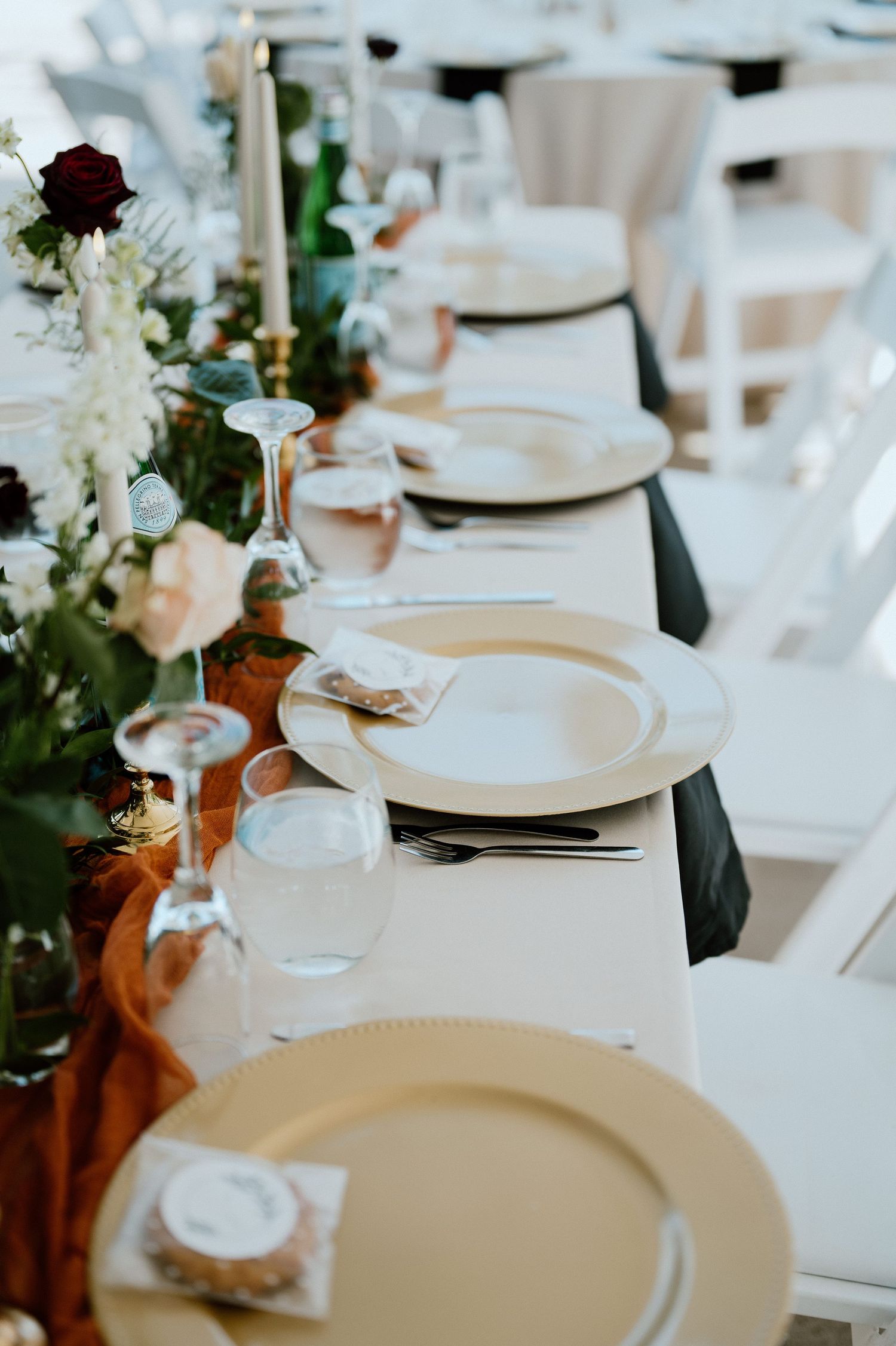 Elegant wedding table setting with white plates, floral centerpieces, and orange table runners.