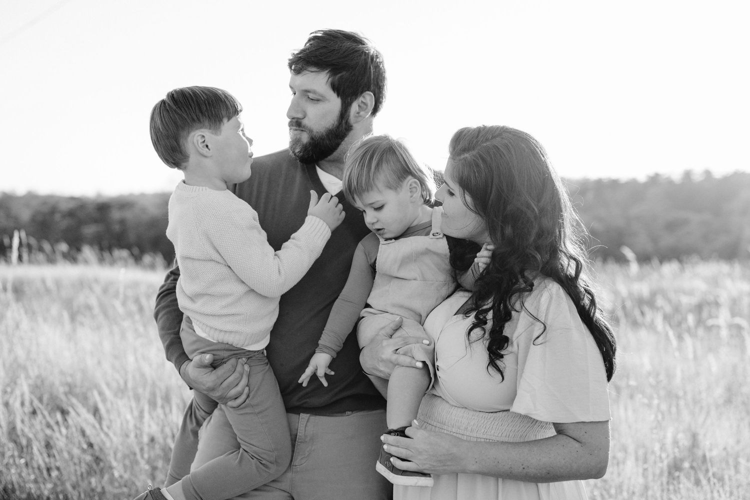 Black and white portrait of family embracing together in field.