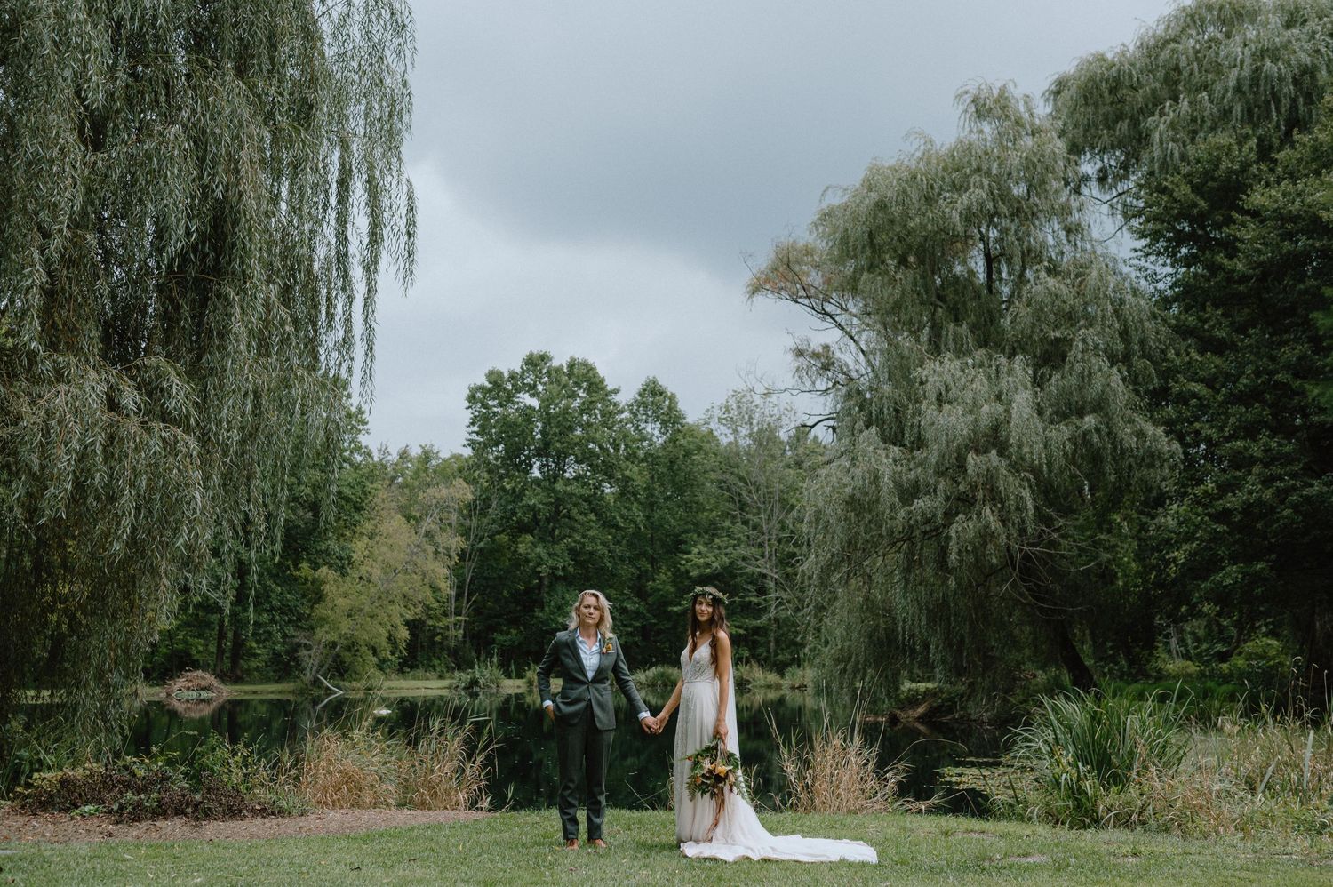 A scenic outdoor wedding portrait beneath drooping willow trees near a peaceful pond.
