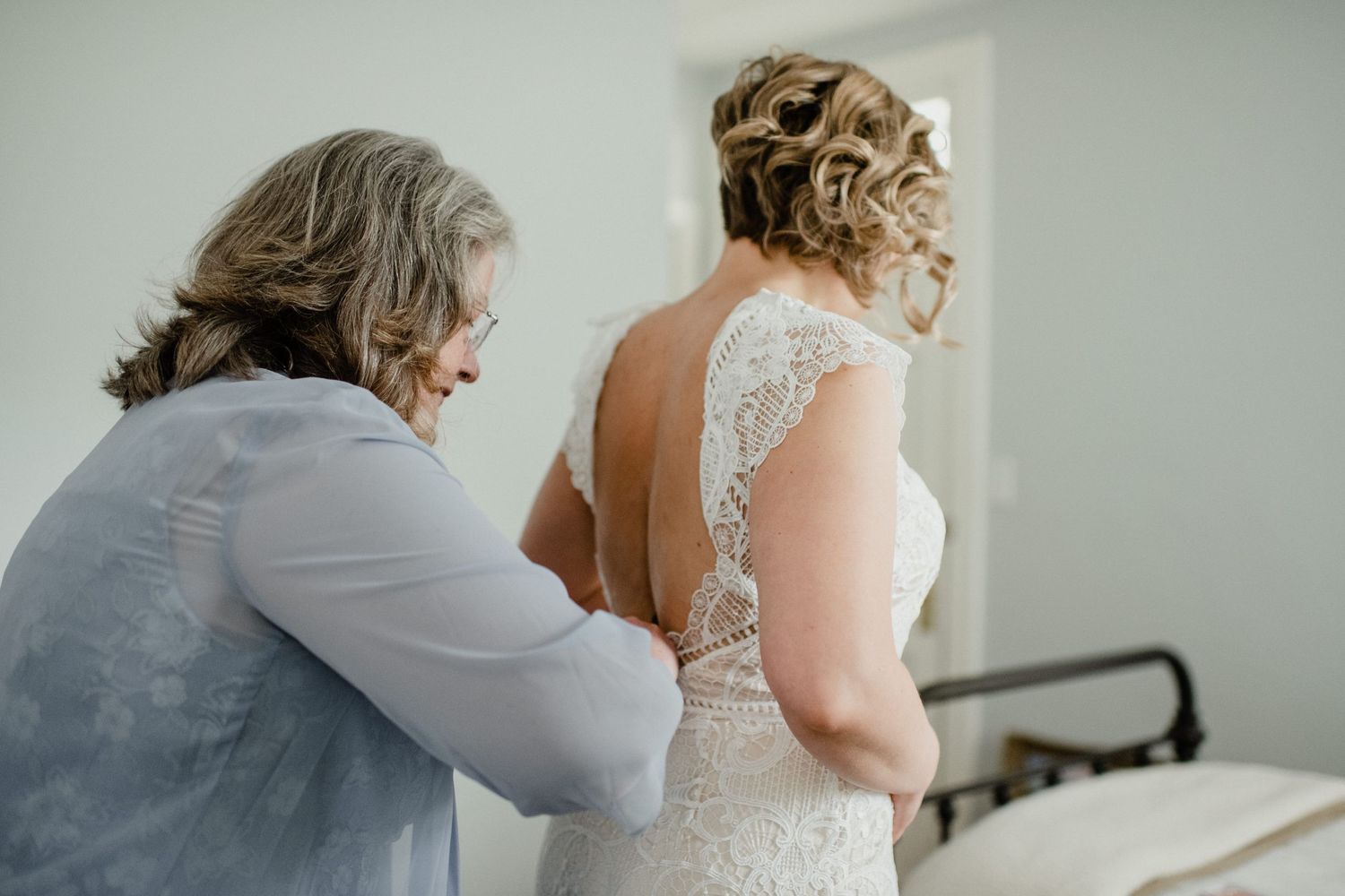 Wedding dress preparation moment in sunlit bedroom.