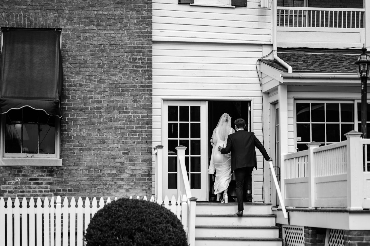 Black and white photo of couple entering doorway of brick building with white trim.