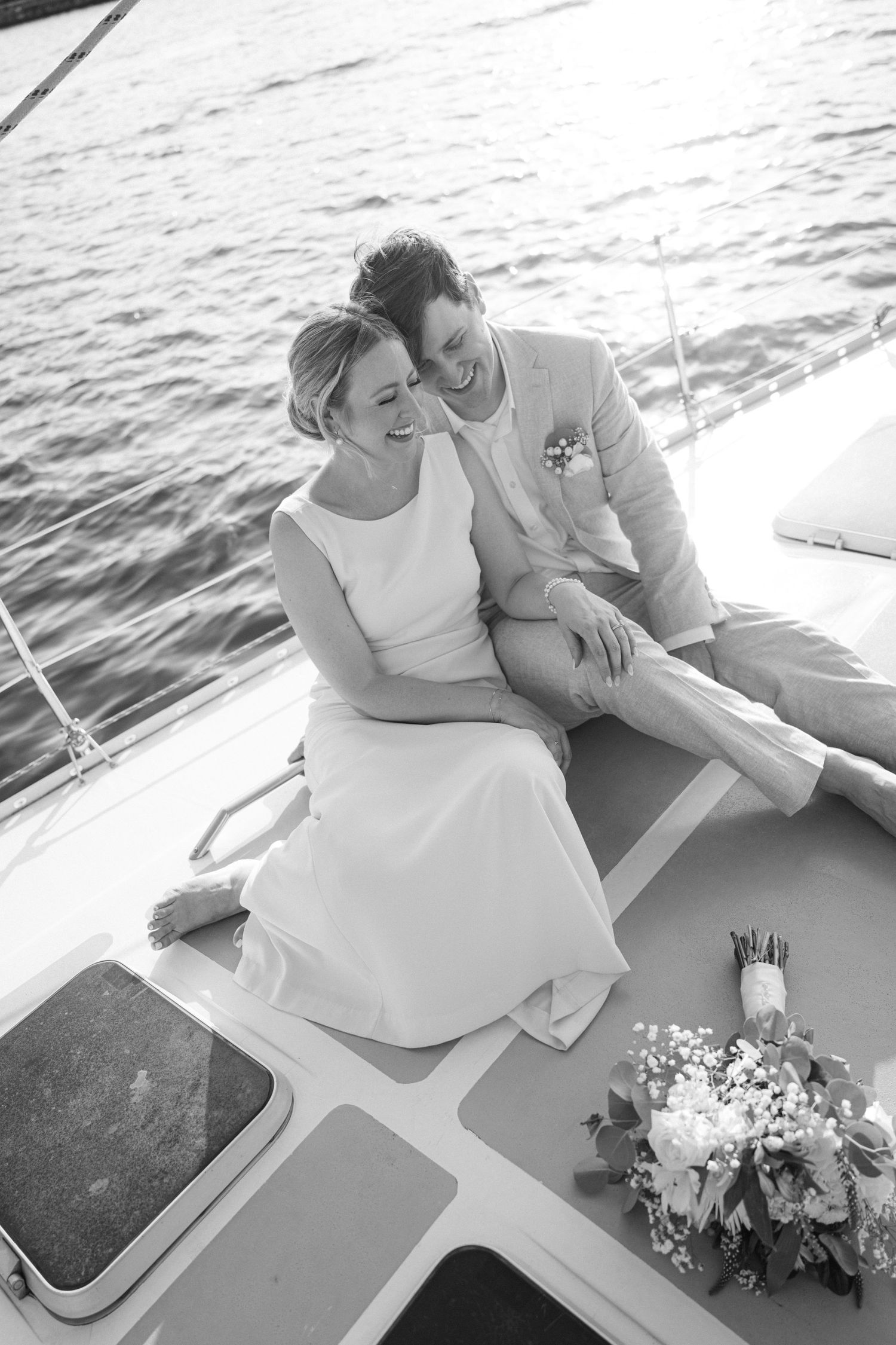 A couple relaxes on a boat with white flowers and elegant wedding attire.
