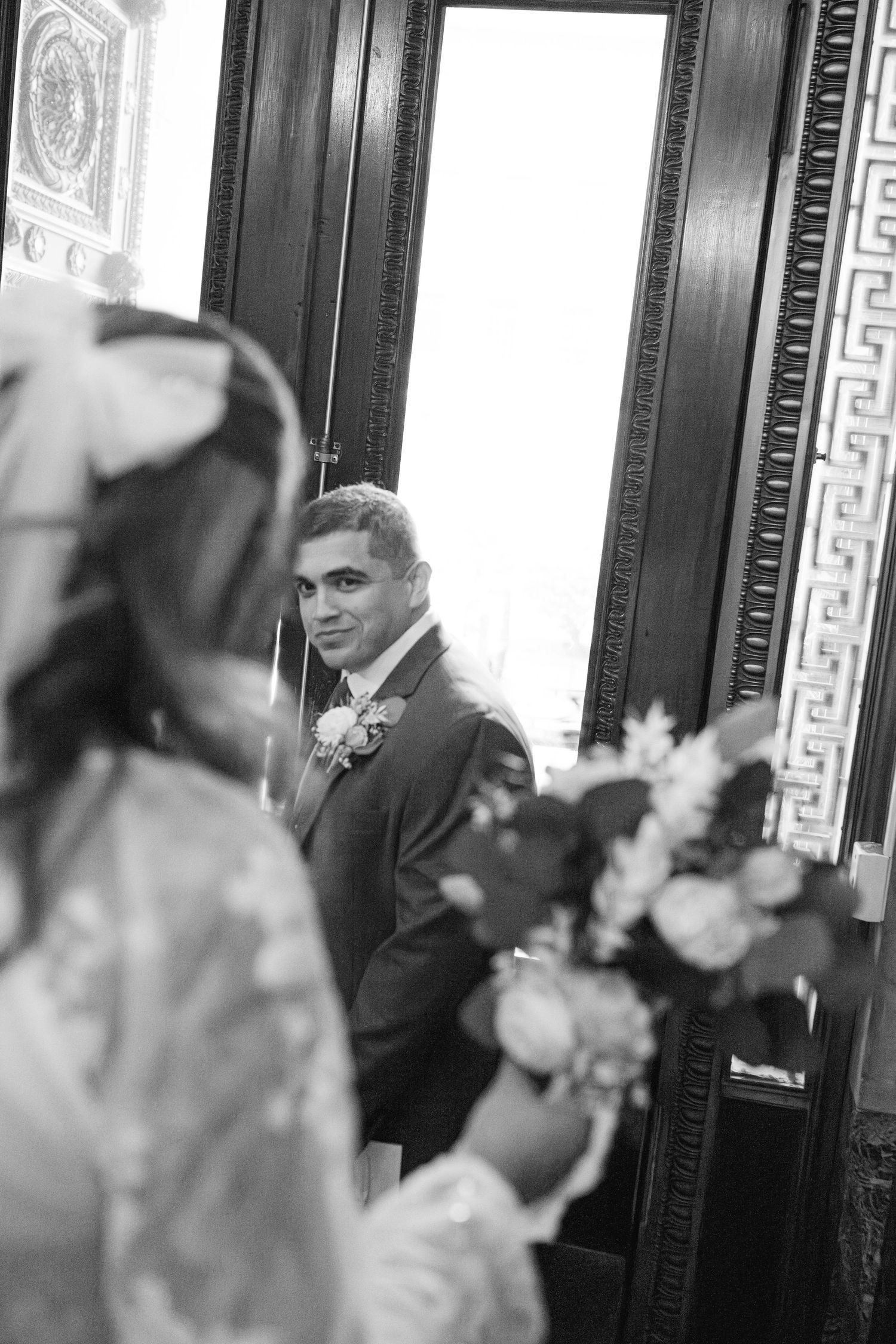 Black and white photo showing guests laughing and socializing at an elegant event with ornate wall details.