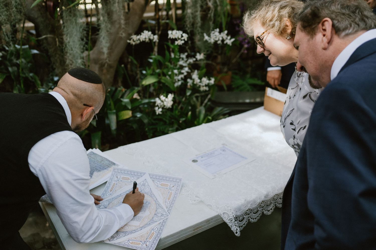 Wedding guests observe as documents are signed at a ceremony table.