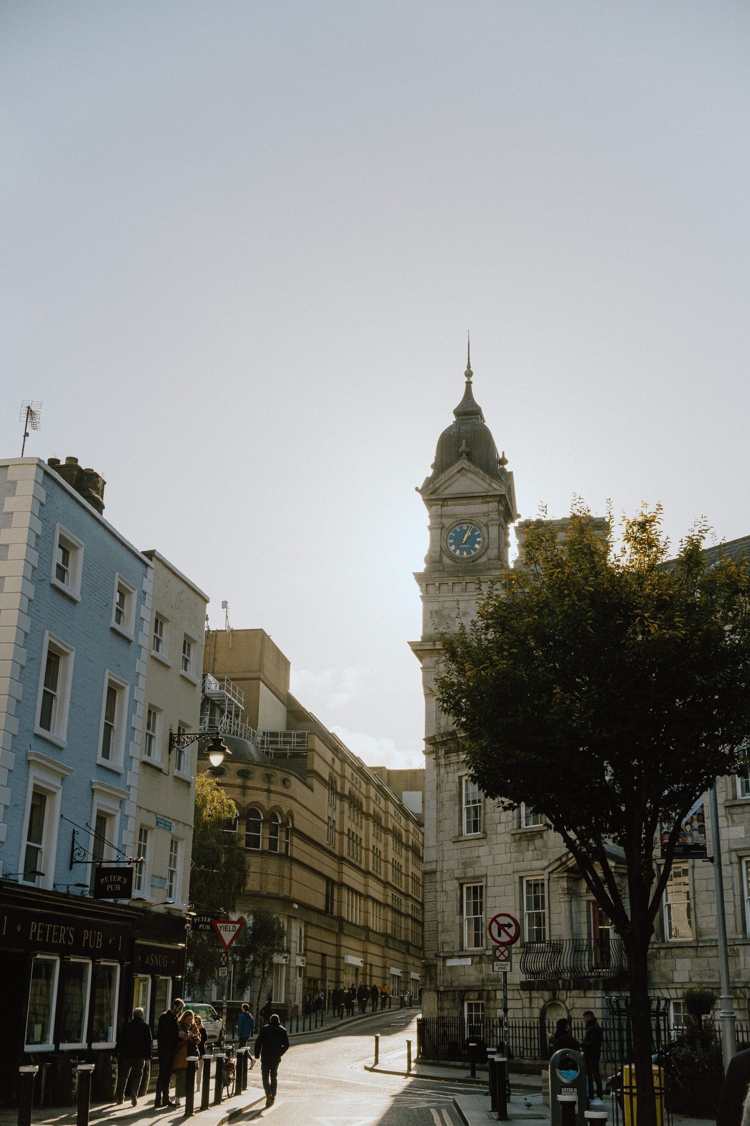 Clock tower and Victorian architecture in an urban setting with sunlit sky.
