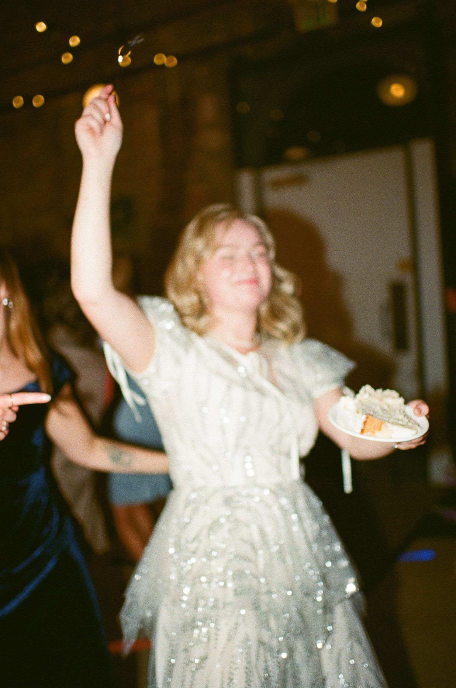Person in sparkly white dress dancing with raised arm while holding a plate.