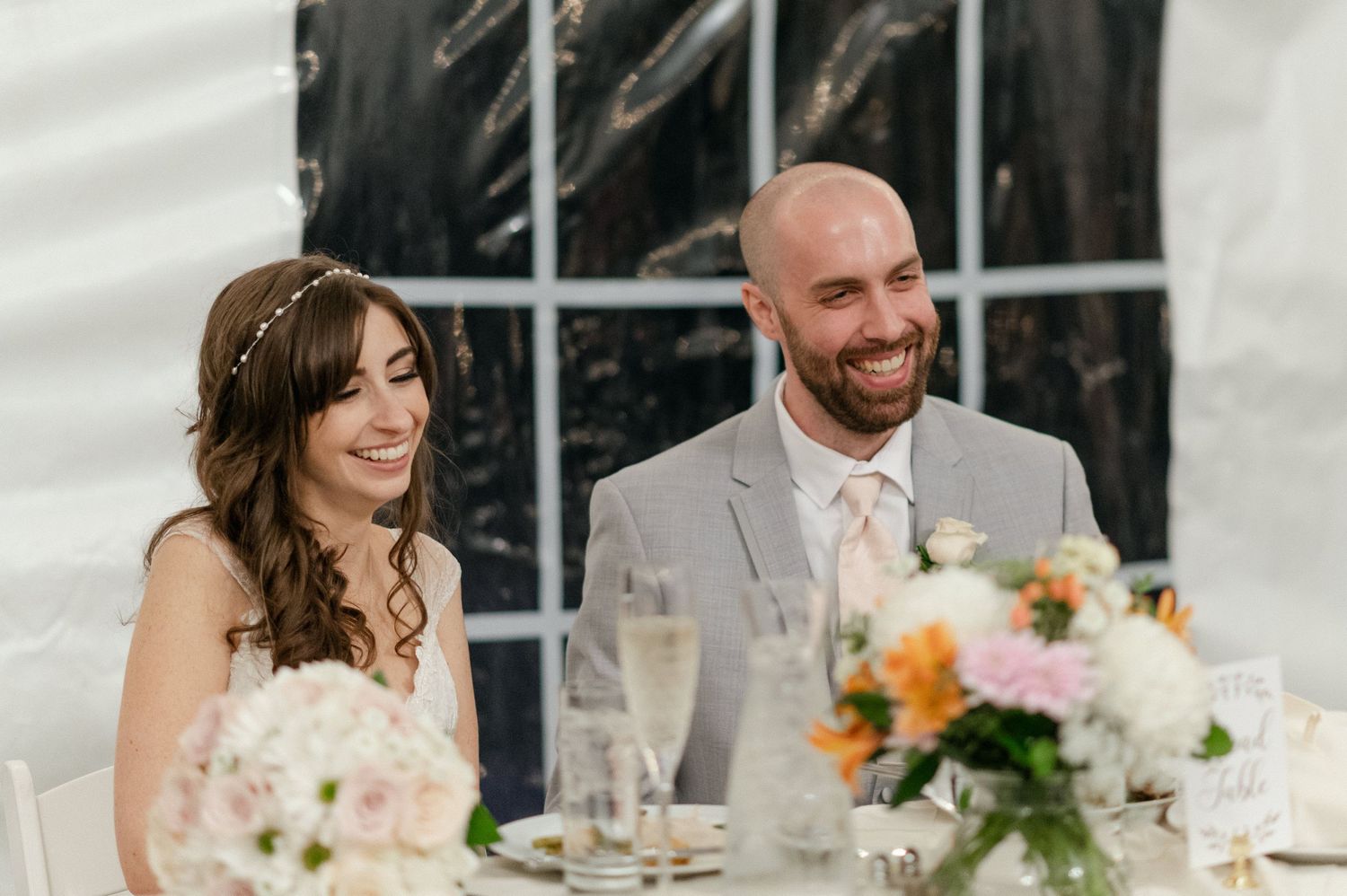 Couple seated at decorated wedding reception table with floral centerpieces.