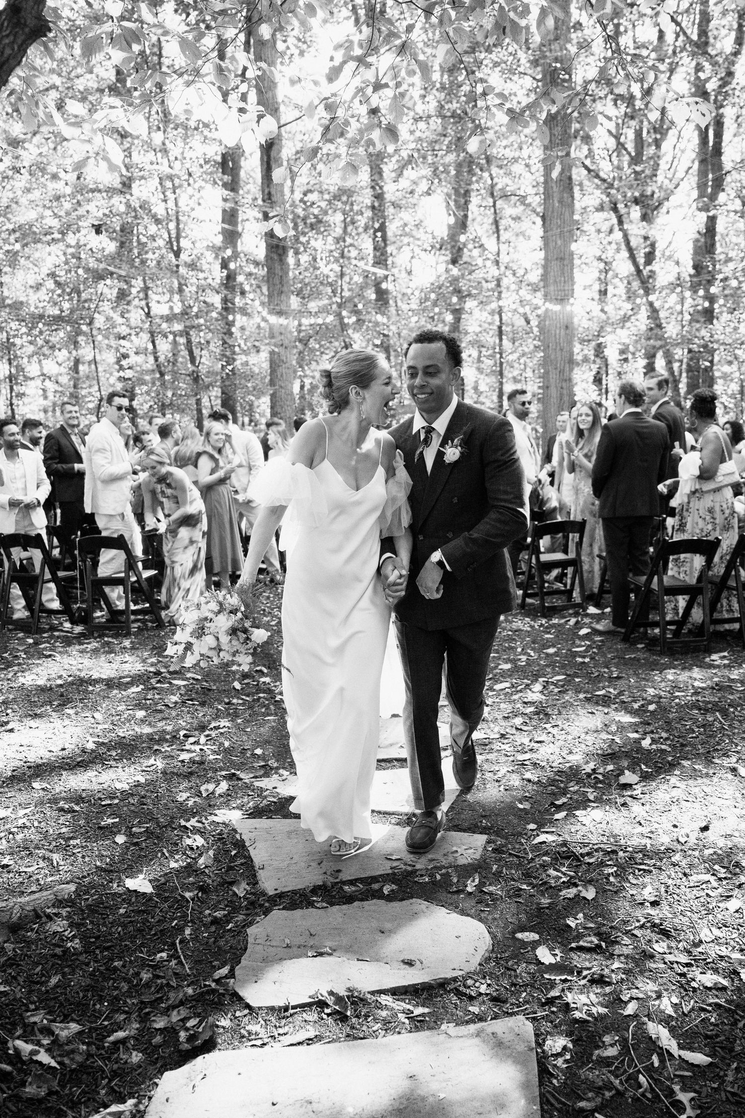 A couple walks together along stone stepping stones after their forest wedding ceremony.