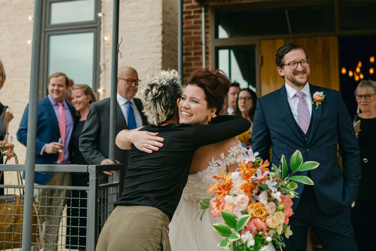 A joyful moment captured during a wedding celebration with guests gathered outside a venue.